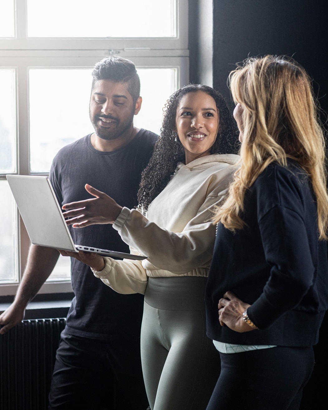 Three people standing by a window collaborating with a computer.